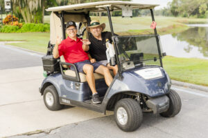 2 golfers in their kart, all smiles, at the FLAGGL conference golf tournament in Orlando
