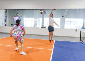 2 pickleballers on the court, one jumping to hit the ball